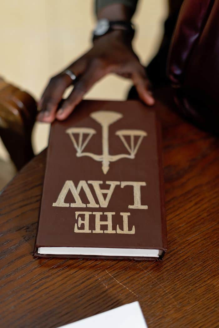 about-img-01 A close-up of a hand holding a law book on a wooden table, emphasizing legal studies.